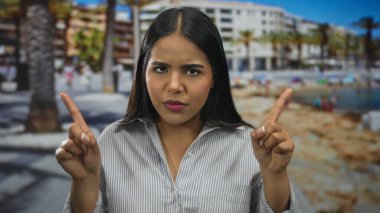 Sahilde kamerayı gösteren parmaklarını kaldıran kadın, deniz kenarındaki gezinti alanında Latin kökenli genç bir Latin tavır sergiliyor..