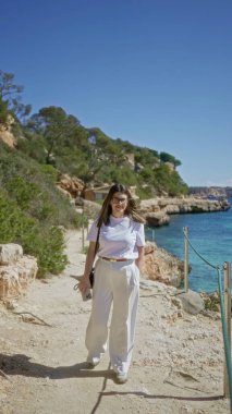 Mallorca 'daki Cala Lombars plajını keşfeden kadın berrak Akdeniz suları ve güneşli bir gökyüzünün altındaki kayalık uçurumlar ile İspanya' da güzel ve huzurlu bir yaz manzarası yaratıyor..