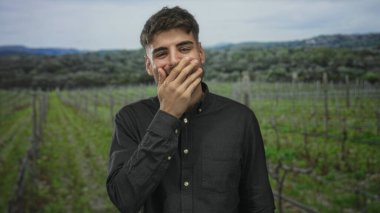 Çiçekli yeşil üzüm bağında bir sıra üzüm tarafından gülümseyen ve yanağına dokunan İspanyol genç adam; dinginlik..