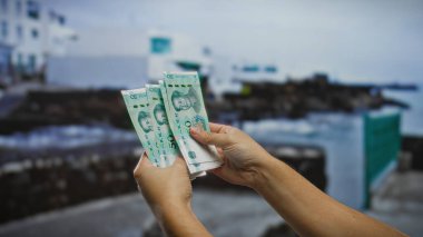 Bir şehir caddesinde Çin yuan banknotları tutan bir adam, şehir ortamında para sergiliyor, finans ve iş temalarını vurguluyor.