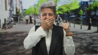 Kadın, şehir caddesinde sessiz kalmak için kanal kenarındaki ağzı eliyle kapatıyor. Şok gizlilik güvenilirliği uyarısı..