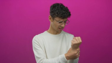 Genç İspanyol bir adam pembe bir stüdyoda yüzünü buruşturuyor ve bileğini sıkıyor..