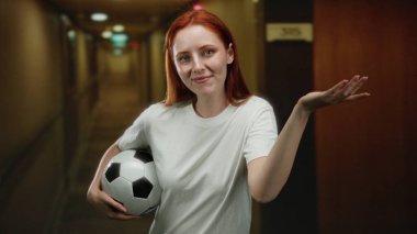 Otel koridorunda elinde futbol topu tutan, kendine güvenen bir kadın..