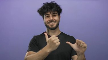 Sakallı, neşeli ve kendinden emin bir ruh hali taşıyan, canlı mor bir arka plana karşı baş parmaklarıyla gülümseyen ve jestler yapan İspanyol genç bir adam..