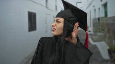 Dar bir sokakta el pençe divan dinleyen kep ve cübbe giyen mezun bir kadın..