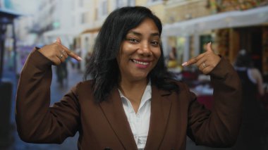 Kahverengi takım elbiseli ve beyaz gömlekli kadın, yoğun şehir caddesinde kendini işaret ediyor..