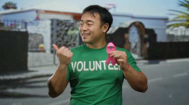 Pembe kurdeleli ve gönüllü tişörtlü genç adam, şehir sokaklarında meme kanseri farkındalığını destekliyor.