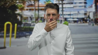 Meşgul şehir caddesinin yaya geçidinde beyaz tişört giyen İspanyol adam ağzını eliyle kapatıyor. Sürpriz..