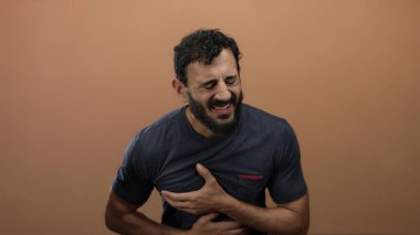 Portakal rengi arka planda gözleri kapalı göğüs ağrısı çeken İspanyol bir adam. Güçlü bir duygusal rahatsızlık yaşıyor..