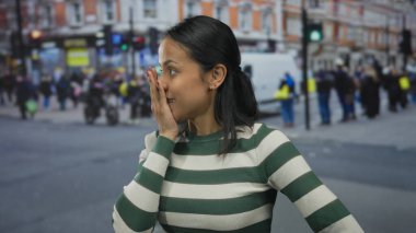 Renkli binalar ve hareketli kalabalıkla caddede dikilen kadın şehir ortamında duygularını gösteriyor ve çizgili kıyafetler giymiş genç bir bireye odaklanıyor..