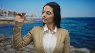 Amerikalı bir rozeti olan takım elbiseli İspanyol bir kadın açık mavi gökyüzü altında parlak bir gülümseme sergiliyor. Kıyı profesyonelliğini ve uluslararası bağlantıyı somutlaştırıyor..