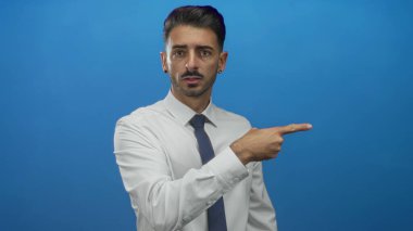 Resmi gömlekli ve kravatlı genç adam stüdyoda görülmemiş bir nesneyi işaret ediyor mavi bir duvara odaklanmış bakışla; dikkat odaklanma azmi.