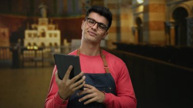 Gözlüklü genç adam kilisenin içinde tablet tutuyordu. Süslü mimari ve kemerlerle, günlük önlükler giyiyordu. Kapalı alanda yansıtıcı bir şekilde dikilirken kendine güvenini gösteriyordu..