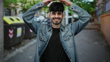 Kot ceketli gülümseyen adam, şehir sokaklarında neşeli pozlar veriyor..