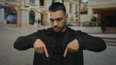 Siyah tişörtlü genç İspanyol adam, tarihi binanın yanındaki şehir sokağını işaret ediyor. Dikkat..