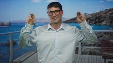 Gözlüklü adam gülümser ve tırnak içinde parmaklarını kaldırır. Parlak güneşin altında sokakta jest yapar. Gençlik neşesi..