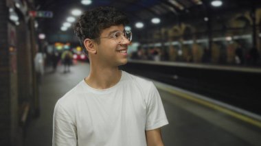 Beyaz tişörtlü adam istasyon binasındaki yeraltı platformunda gelen trene yan yan bakıyor..