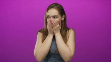 Genç beyaz kadın stüdyoda gülümserken iki eliyle ağzını kapatıyor. Sürpriz..