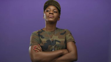 Kamuflaj üniformalı kadın stüdyoda askeri künyeleri gösteren kollarını çaprazlıyor ve metanetli bir ifadeyle ileri bakıyor..