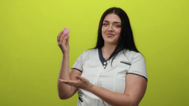 Kadın, kadınsı bakımı ve yetkilendirmeyi vurgulayan canlı sarı arka plana karşı güvenilir bir adet bardağı sunar..