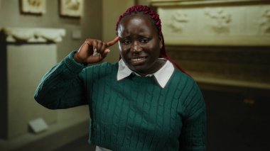 Müzenin içinde el kol hareketi yapan bir kadın, eski eserlerle çevrili, neşeli bir delilik duygusunu ifade ediyor, düşünceli bir ifade ve günlük kıyafetle, tuhaf bir atmosfer yaratıyor..