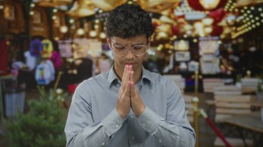 Sarkan ışıklar altında sokak pazarında dua eden, elleri sımsıkı bağlı gözlük takan bir adam..