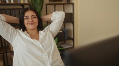 Raflar ve bitkilerle çevrili rahat bir ifadeyle modern ofiste uzanan bir kadın iş için rahat bir iş yeri sergiliyor..