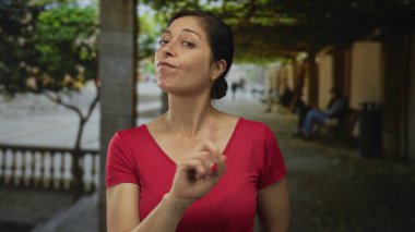 Kırmızı tişörtlü İspanyol orta yaşlı kadın sokakta sıralanmış sıraları işaret ediyor..