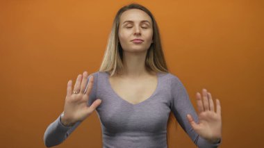 Gözleri parlak turuncu arka planda meditasyon yapan bir kadın sakin tavırlar sergiliyor ve izole bir ortamda rahatlıyor..