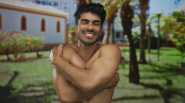 Palmiye ağaçları ve otlarla çevrili yeşil çerçeveli bir binada çıplak kollarıyla çıplak omuzlarını saran İspanyol genç adam..