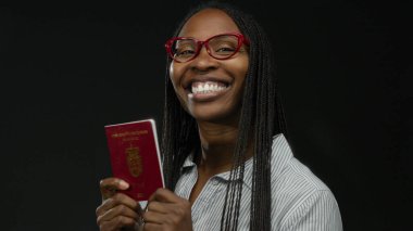 Siyah arka planda Danimarka pasaportu taşıyan kırmızı gözlüklü ve çizgili tişörtlü neşeli bir ifade sergileyen bir kadın..