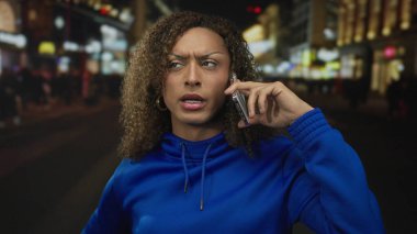 Mavi kapüşonlu kadın gecenin bir yarısı kalabalık neon ışıklı şehir sokağında akıllı telefonu kulağına tutuyordu..