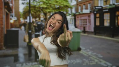 Beyaz kolsuz tişörtlü İspanyol kadın. Yumruğu sıkılmış, orta parmağı uzatılmış ve kaşları çatık. Öfke..