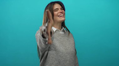 İzole edilmiş yeşil duvara doğru gülümseyen ve elini uzatan kadın, günlük kıyafetler giymiş, yakınlık ve samimiyeti öneriyor.