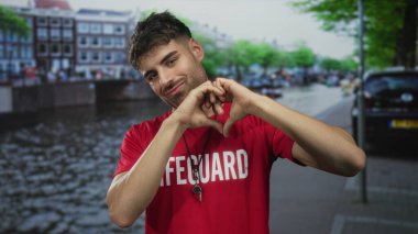 Kanal caddesinde elleri ile kalp hareketi yapan kırmızı tişört giyen genç İspanyol cankurtaran..