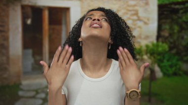 Kadın kıvırcık saçlarını savurur ve her iki elini de kaldırır. Kızgın bir şekilde taş evin girişinde, gökyüzüne bakar. Hayal kırıklığı..