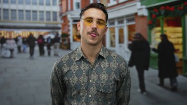 Kalabalık bir şehir caddesinde gözlüklü, hareketli insanları hareketli gösteren canlı bir mimariyle çevrili genç İspanyol bir adam açık havada hareketli bir ortam yaratıyor.