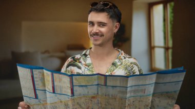 Yatak odasında haritası olan tropikal gömlek giyen genç adam pencereden güneş ışığıyla gülümsüyor. Geziye hazırlanmayı ve dışarıda macera yaşamayı öneriyor.