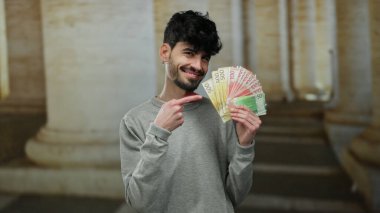 Norveçli Krone 'u elinde tutan adam eski bir üniversitede açık havada para yatırıyor, akademik bir ortamda kendine güvenen bir ifadeyle para gösteriyor..