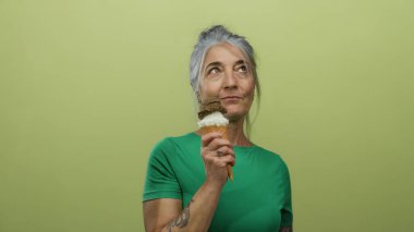 Gri saçlı yaşlı kadın, büyüleyici modern ortamda canlı sarı bir arka plan karşısında dondurma külahını seviyor, mutluluk ve yaz havası yayıyor..