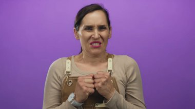 İzole edilmiş mor bir arkaplan üzerine önlük giyen kadın duygularını ifade eden yüz hatlarıyla ifade eder, dinamik ve canlı bir anı yakalar..