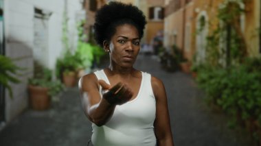 Beyaz kolsuz tişörtlü bir kadın, elini şehir sokaklarında gezdirip, şehir hayatını, ifadesini ve nişanını gösteriyor..