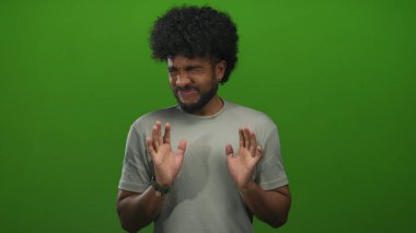 Yeşil arka plan önünde tiksindiğini ifade eden bir adam, kapalı alanda izole edilmiş, günlük gri bir gömlek giyen, duygusal, anlamlı, esprili ve komik bir tepki gösteren bir adam..