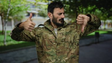 Üniformalı İspanyol askeri bir adam açık havada baş parmak işareti yapıyor, ilginç bir açık hava ortamında farklı görüşleri yansıtıyor..