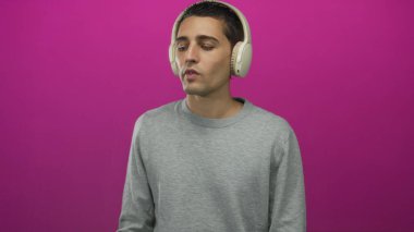 Kulaklıkla müzik dinleyen genç bir adam canlı pembe bir arka plana karşı, eğleniyor ve rahatlıyor..