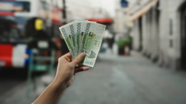 Güney Koreli bir adam açık hava otobüs durağında elinde para ve kentsel geçmişiyle gelişigüzel bir şehir anını yakalıyor..