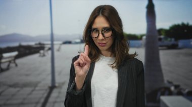 Açık gökyüzü ve okyanus manzaralı güneşli bir sahil geçidinde, gözlüklü ve rahat bir sahil atmosferi sergiliyor..