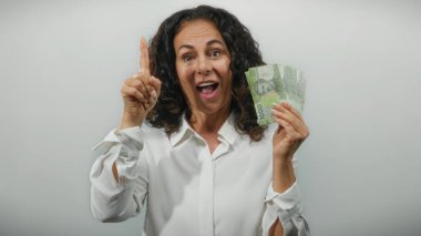 Orta yaşlı kadın elinde Şili pezosu olan beyaz bir arkaplan karşısında düşünceli bir jest yapıyor, finansal kararları ve fikirleri sembolize ediyor.