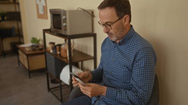 Ofis ortamında dolar banknotlarını inceleyen olgun bir adam, raflar ve arka planda görünen bir mikrodalga fırın..