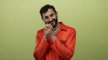 Turuncu tulumlu, sakallı İspanyol bir adam sarı bir arka planda duruyor. El sıkışıyor ve güvenle gülümsüyor..